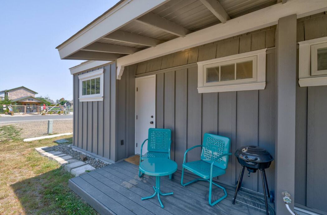 A covered porch with two turquoise chairs and a small table, a grill, and a door with a window.