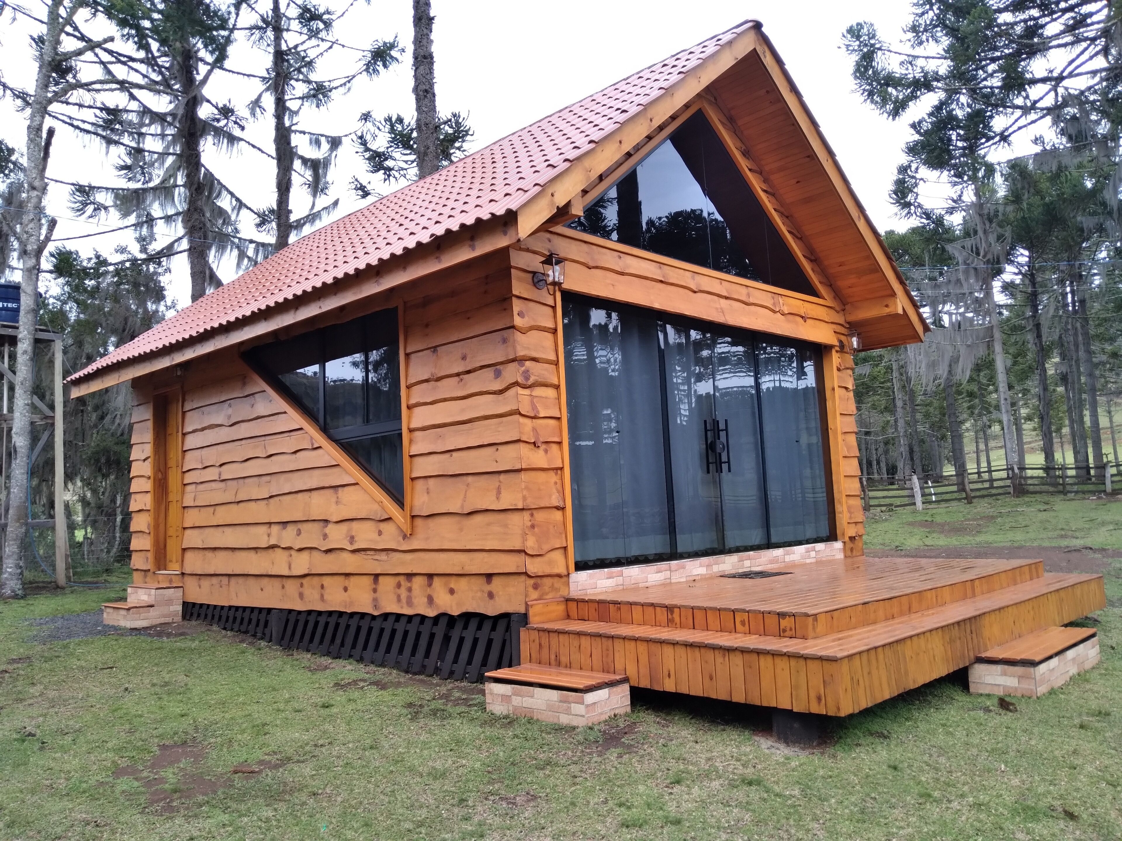 Uma cabana de madeira com telhado inclinado, janelas amplas e um deck de madeira.