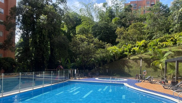A swimming pool with a tiled deck, surrounded by greenery and a fence. - Exclusive condominium ideal for families with babies and pets. (Envigado)