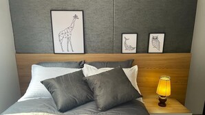 A neatly made bed with a quilted white duvet and grey pillows, a bedside lamp, and framed artwork on the wall. - Exclusive condominium ideal for families with babies and pets. (Envigado)