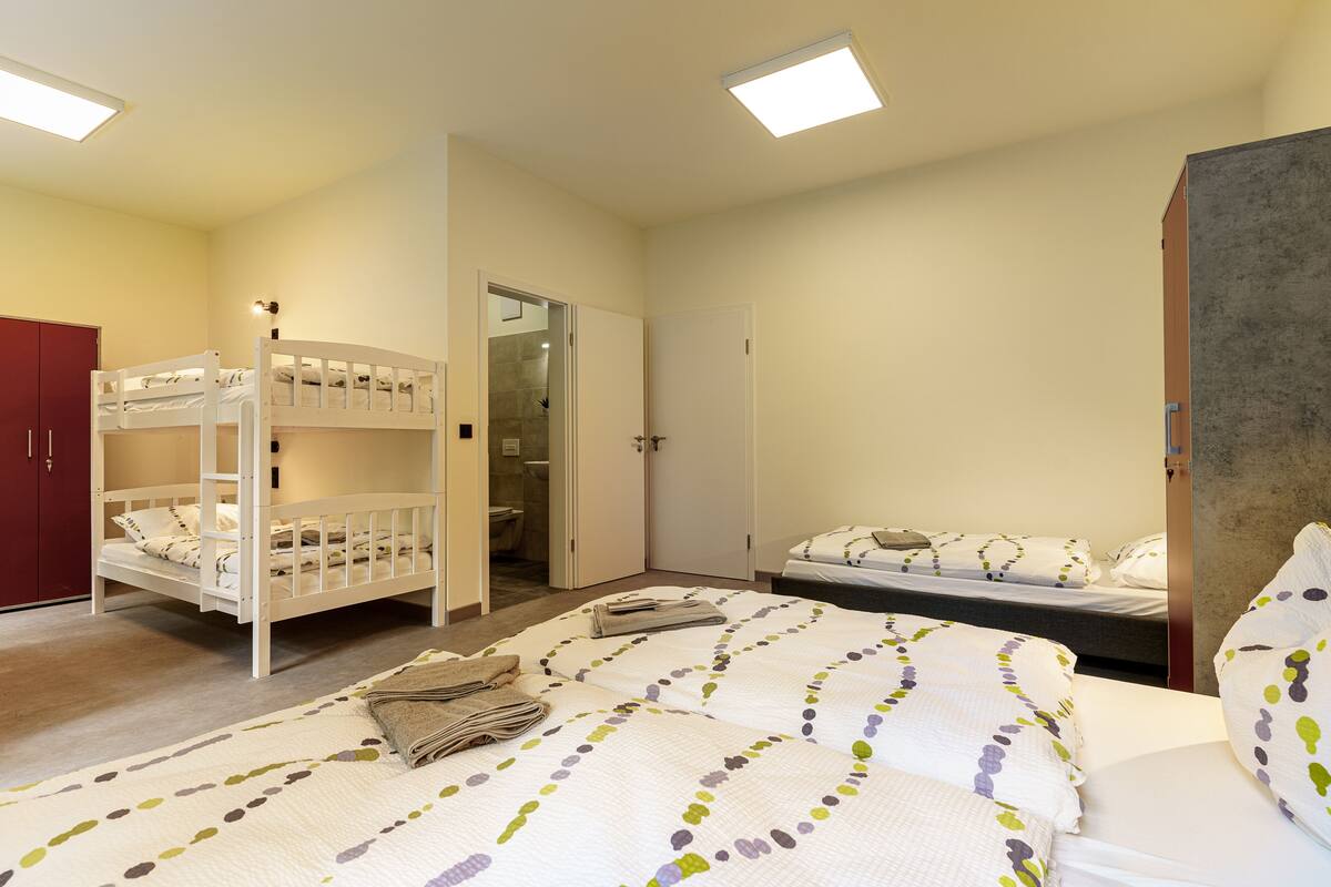 A room with bunk beds, a large bed with a patterned quilt, a wardrobe, and a door leading to a bathroom.