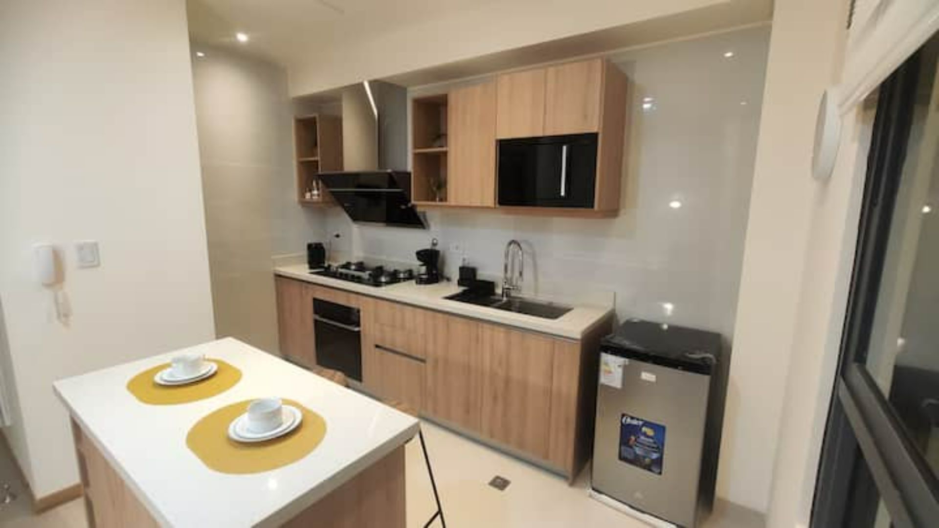 A compact kitchen with wooden cabinets, a black microwave, and a small refrigerator.