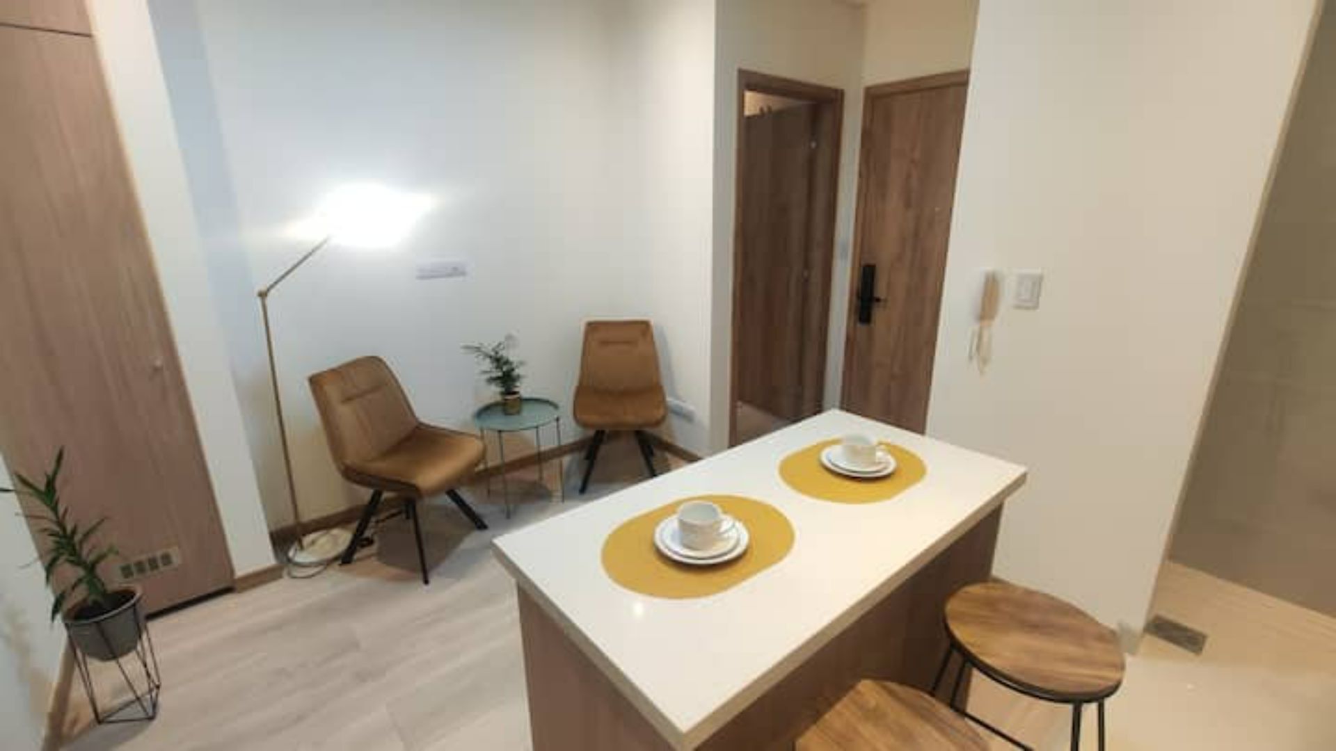Een compacte, moderne keuken met een wit aanrecht, twee stoelen, een tafeltje en een potplant.