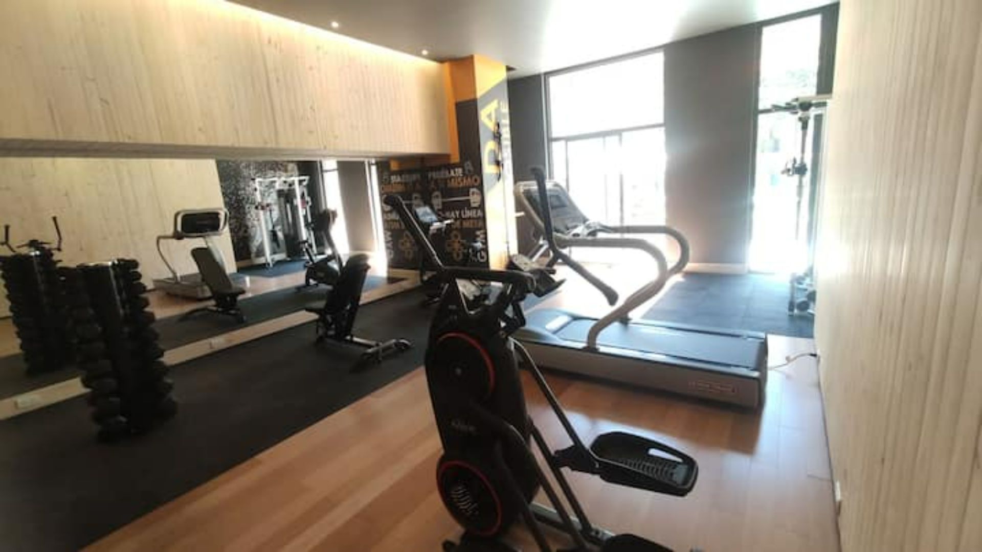 Een fitnessruimte met cardioapparatuur, gewichten en een spiegelwand.