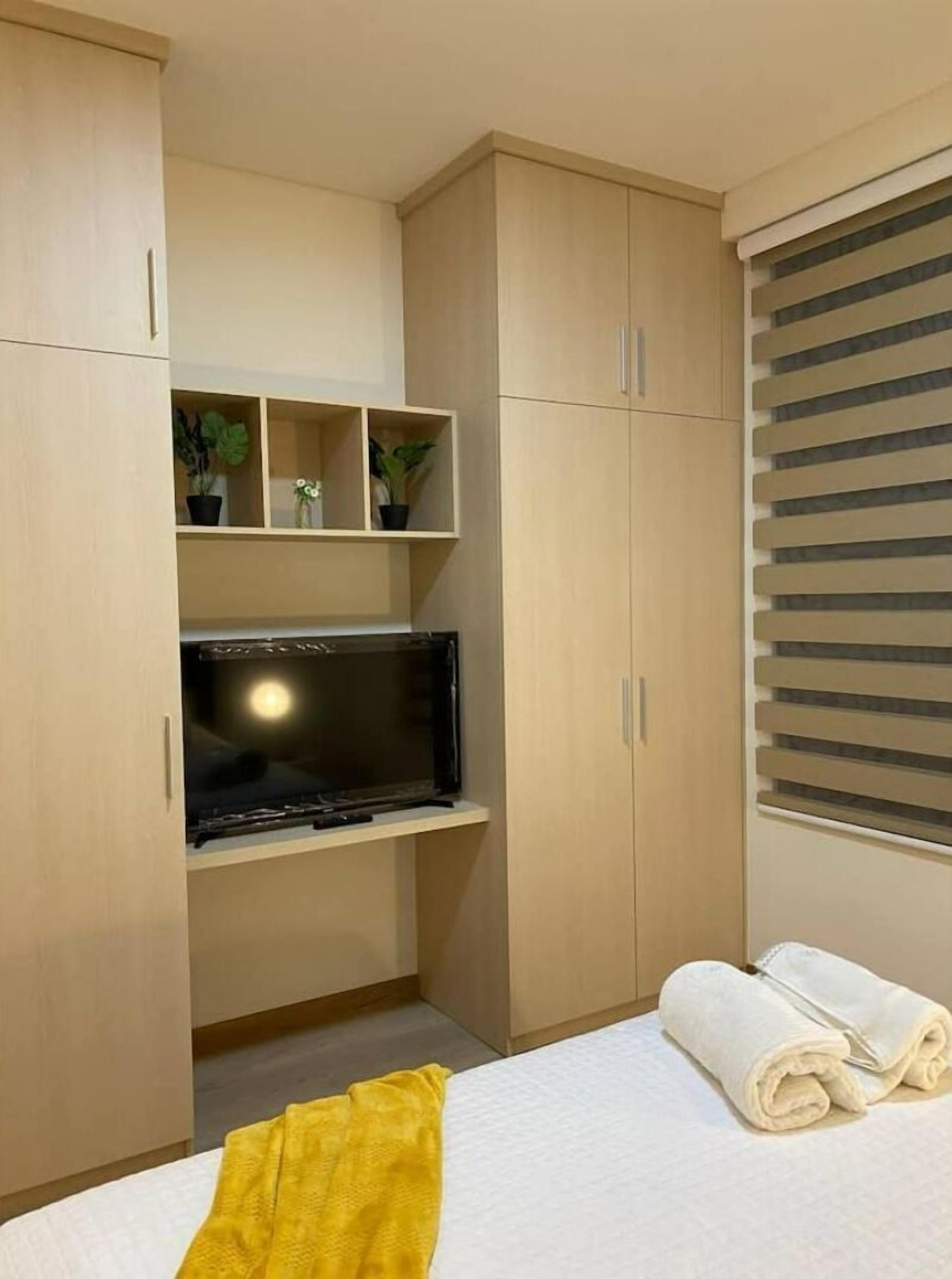 Een slaapkamer met een bed, een televisie, een plank met planten en een raam met zonwering.