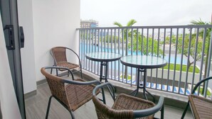 Un balcón con sillas de mimbre y dos mesas de vidrio, con vista a una piscina y follaje.