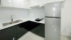 Una cocina moderna con armarios blancos, encimera negra y refrigerador de acero inoxidable.