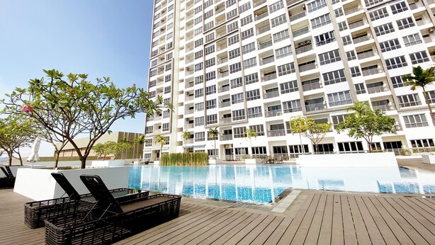 Un edificio alto con piscina, terraza de madera y sillones de descanso.