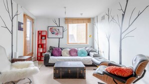 En moderne stue med sofa, lænestol, lille bord og et vindue med persienner.