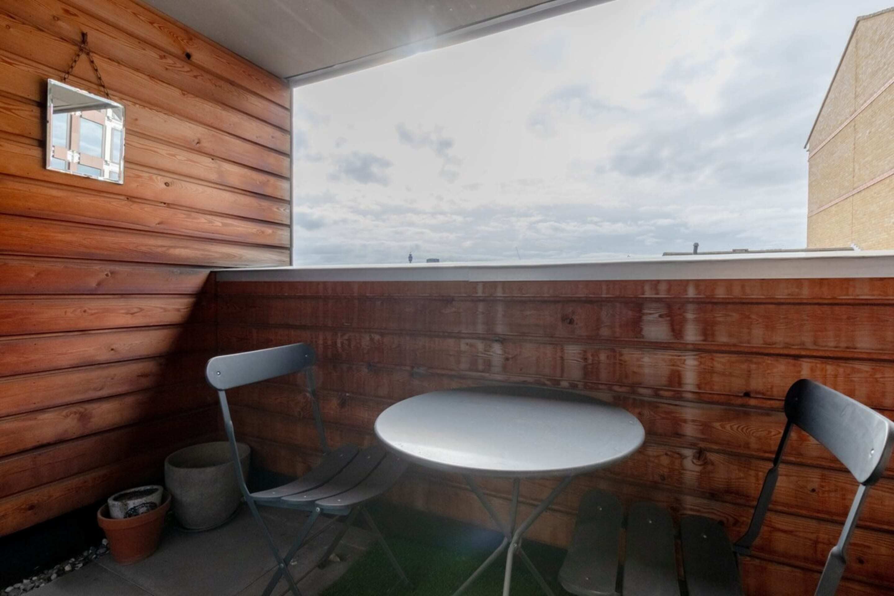 A wooden cabin with a small round table and two chairs, a window, and a view of the sky.