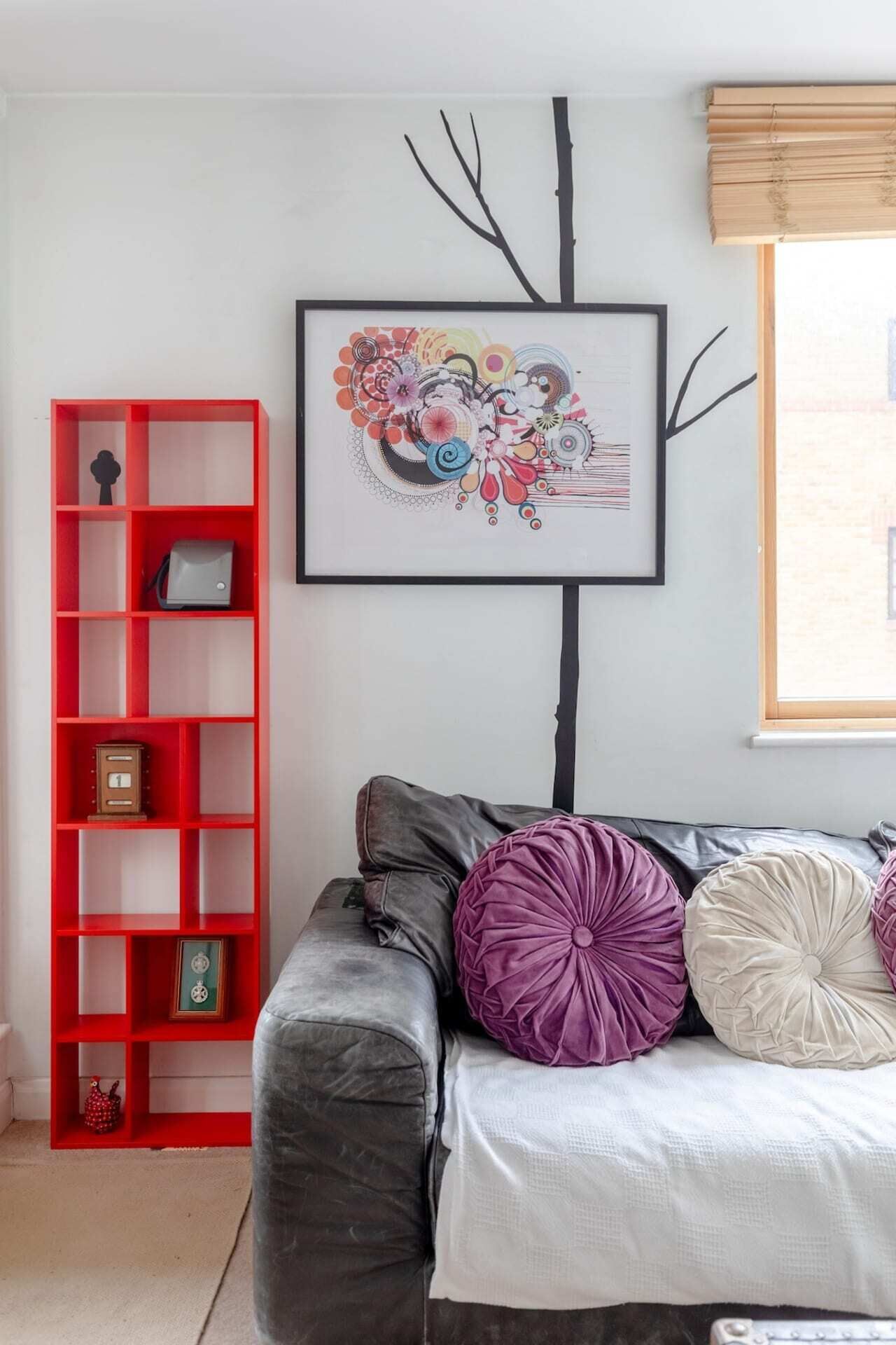 Uma sala de estar moderna com um sofá cinzento, estante vermelha e uma obra de arte abstrata emoldurada na parede.