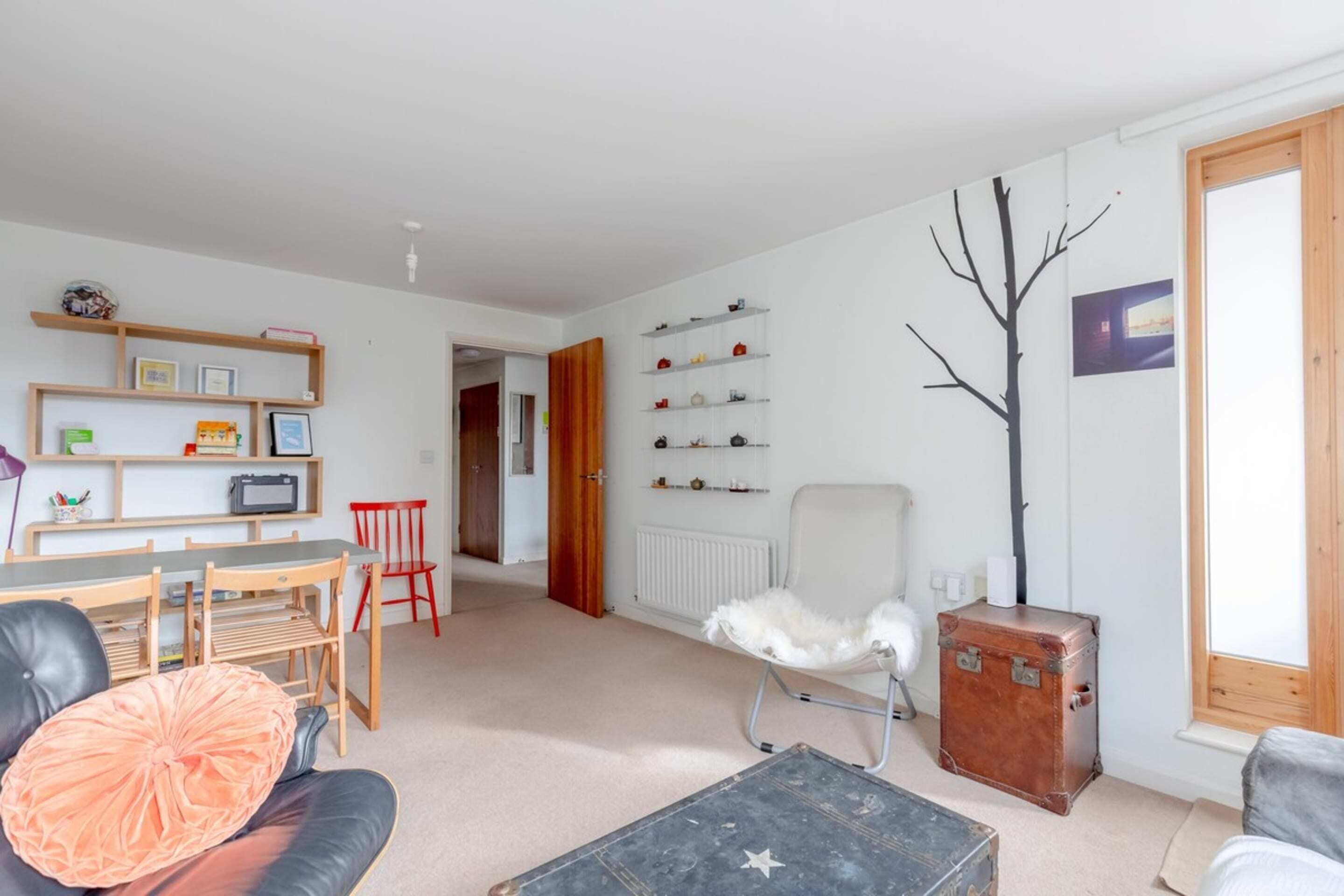 A living room with a sofa, a chair, a table, and a bookshelf. There is a suitcase and a radiator on the wall.