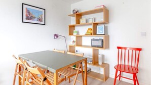 Et værelse med et gråt bord, træstole, en rød stol, en reol og et billede i ramme på væggen.