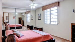 Un dormitorio con un espejo grande, dos camas, un ventilador de techo y una ventana con persianas.