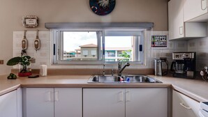 Una cocina con un lavamanos doble, armarios blancos, una cafetera y vistas a edificios.
