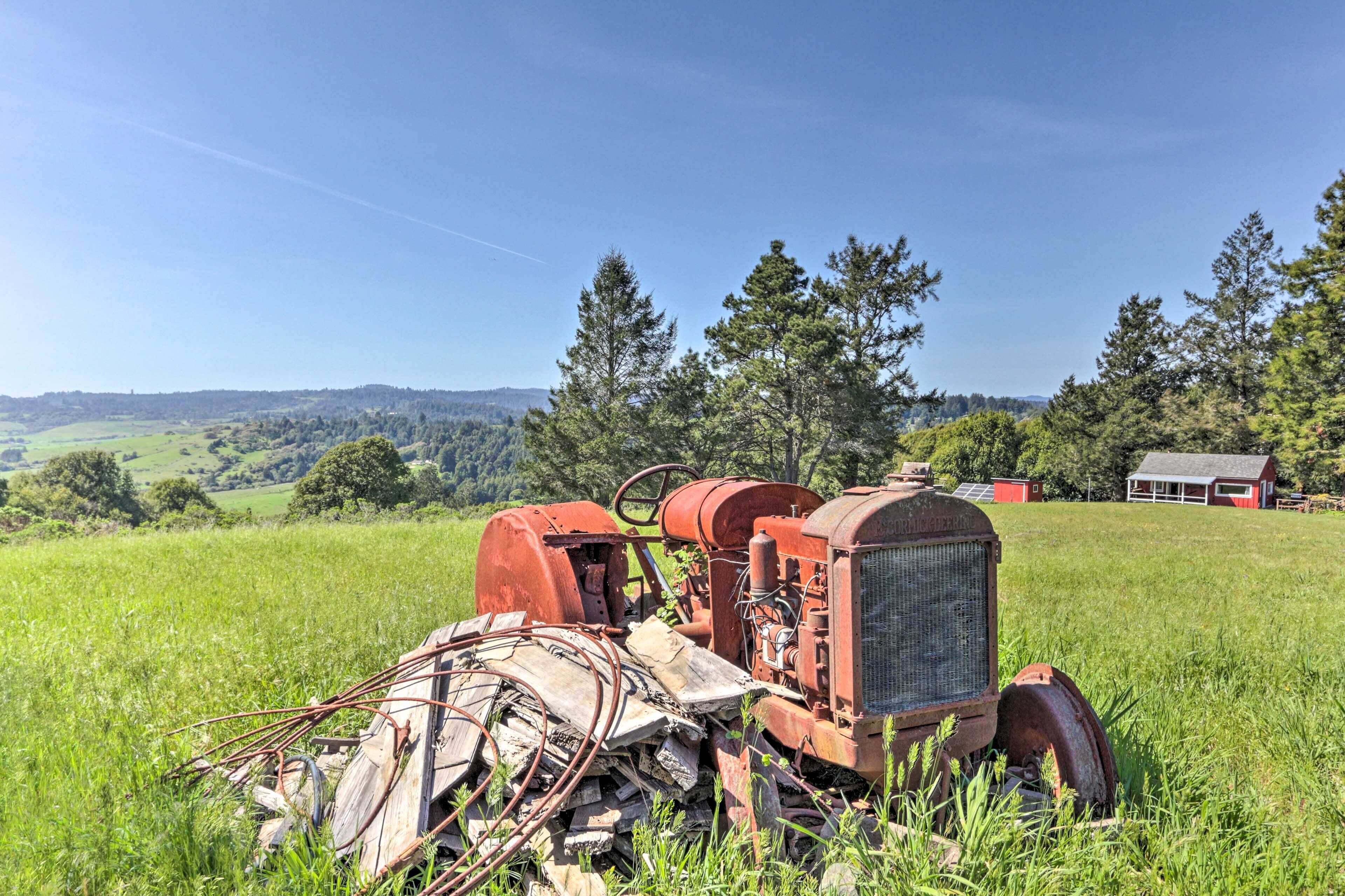 Ein alter, roter Traktor auf einer Wiese, im Hintergrund ein rotes Bauernhaus.