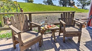 Terraza de madera con dos sillas Adirondack y una mesita baja con aperitivos y una botella.