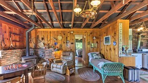 Interior rústico de una cabaña con una mesa de madera, una silla de cuero y un rincón acogedor con una butaca verde y un sofá.