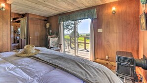 Dormitorio de cabaña de madera con una cama grande, una lámpara rústica y vistas a una terraza de madera y al paisaje.