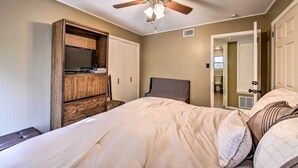 Une chambre à coucher comprenant un lit, une commode en bois, un ventilateur de plafond et une porte donnant sur une salle de bain.