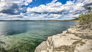 Un paysage côtier caractérisé par une eau claire, une rive rocheuse et une terre lointaine, le tout sous un ciel partiellement nuageux.