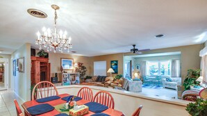 Amplia sala de estar con una mesa de comedor para cuatro personas, un candelabro y vista al comedor contiguo.
