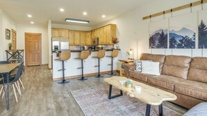 A modern kitchen with wooden cabinets, a refrigerator, and a bar area with stools.