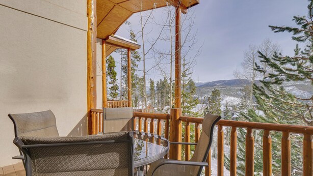 A wooden deck with outdoor furniture, a wooden railing, and a view of snow-covered trees and mountains.