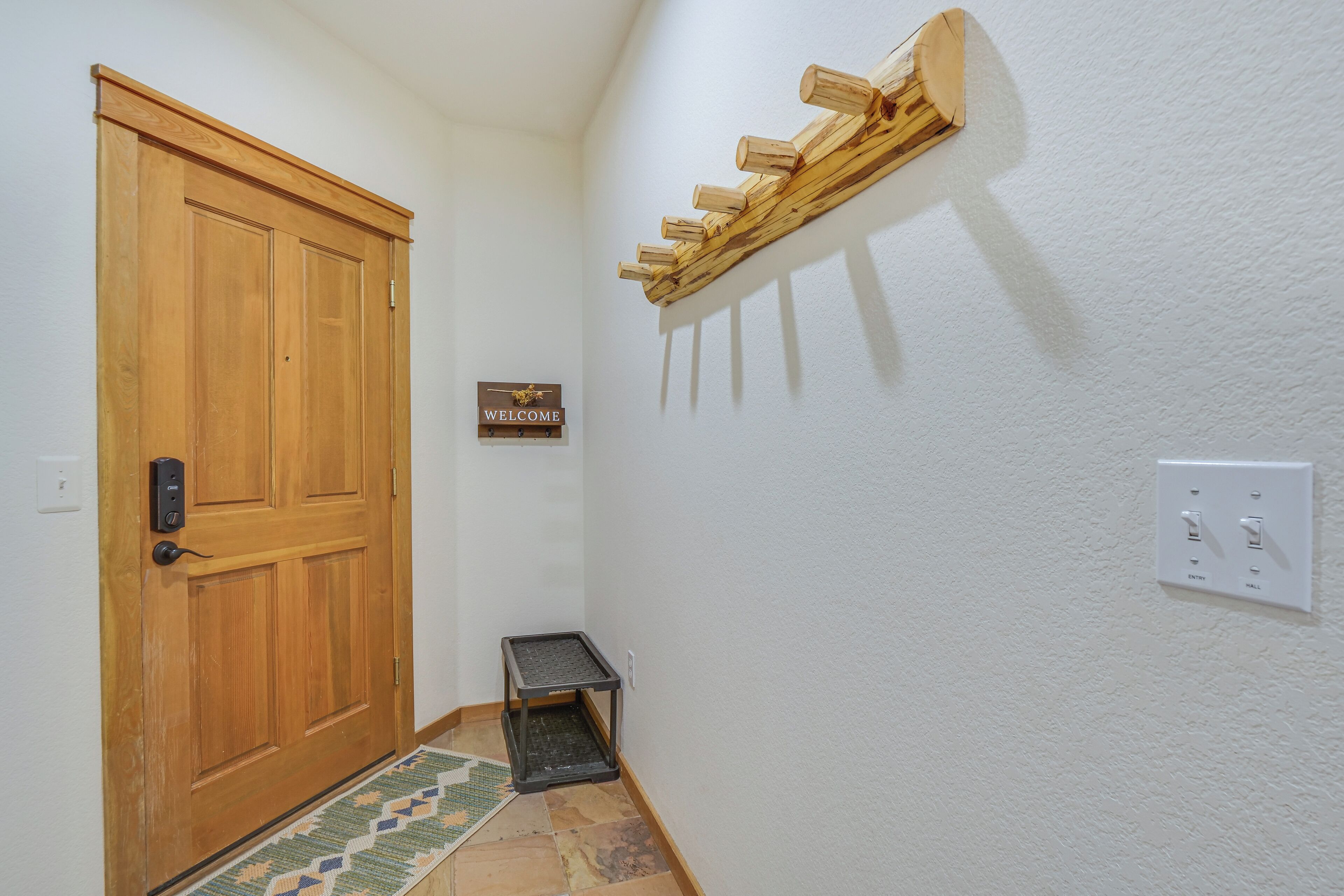 A hallway with a wooden door, a welcome sign, a small table, and a wall-mounted light fixture.