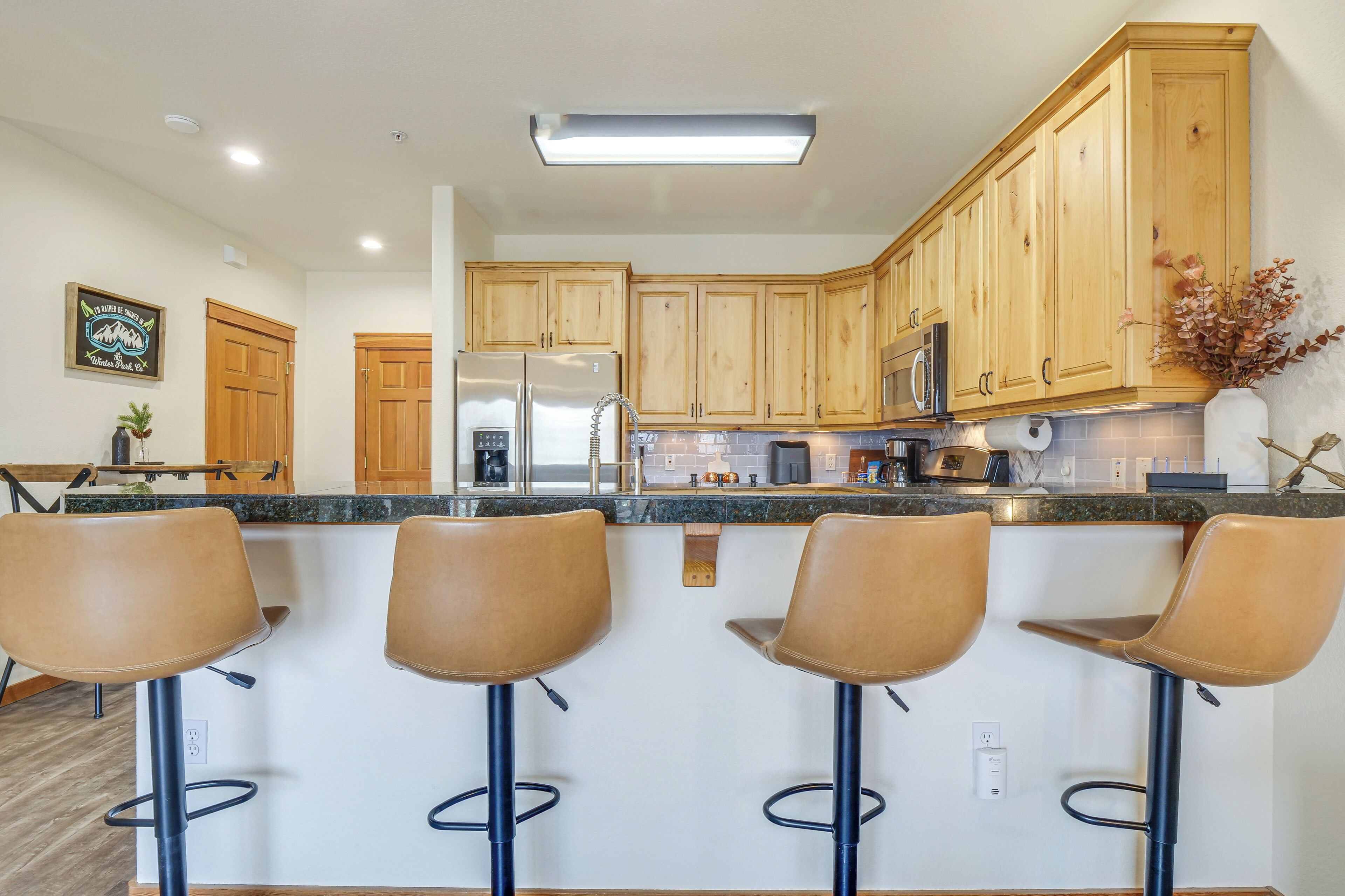 Cocina moderna con armarios de madera, refrigerador de acero inoxidable, microondas y una barra con taburetes.