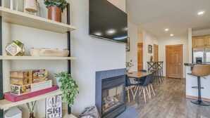 A modern living room with a fireplace, a flat-screen TV mounted on the wall, and a dining area with wooden furniture.