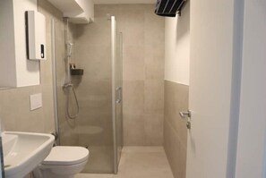 Compact bathroom with a shower enclosure, toilet, and sink.