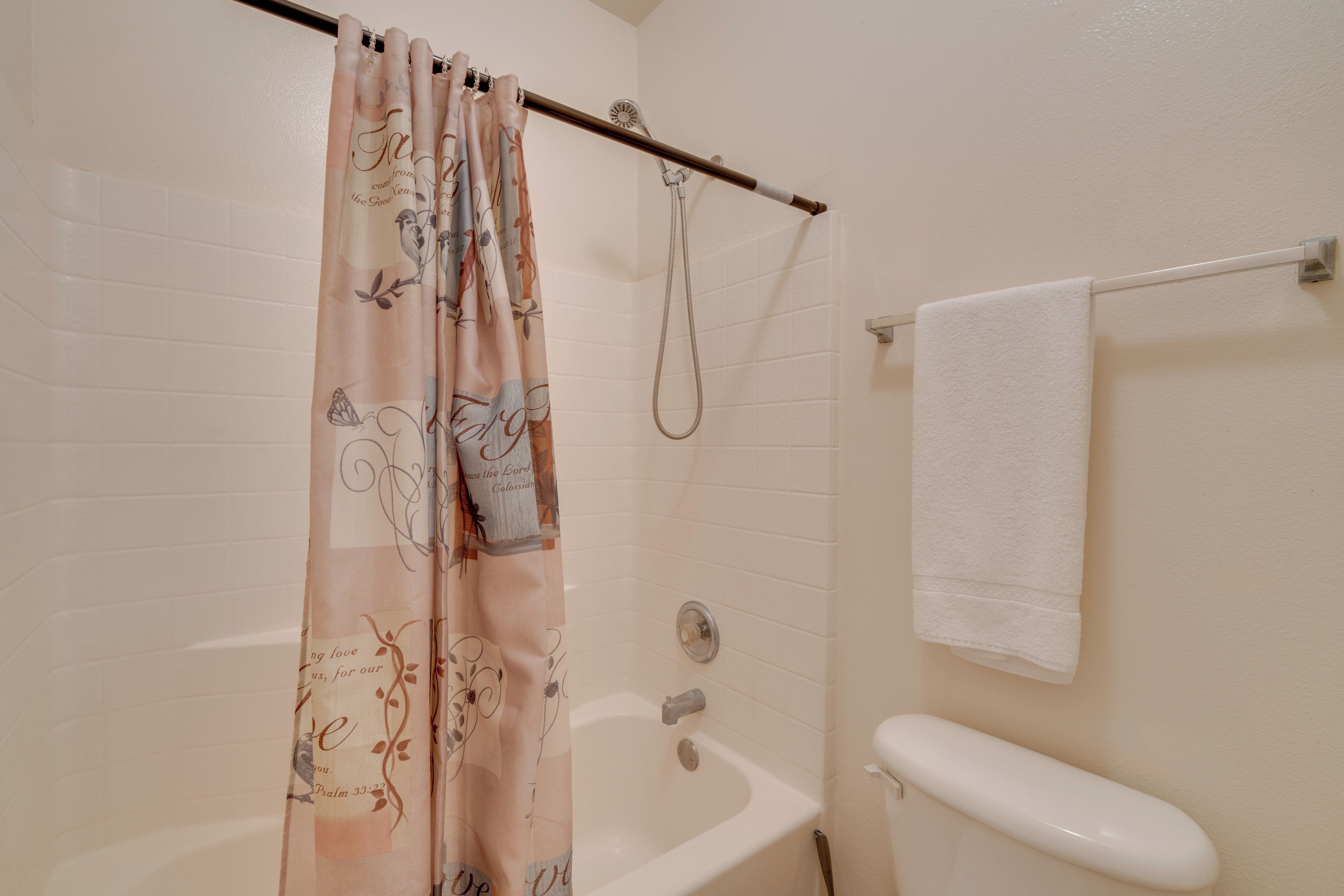 Ein Badezimmer mit Duschvorhang, Badewanne, Handtuchhalter und Toilette.