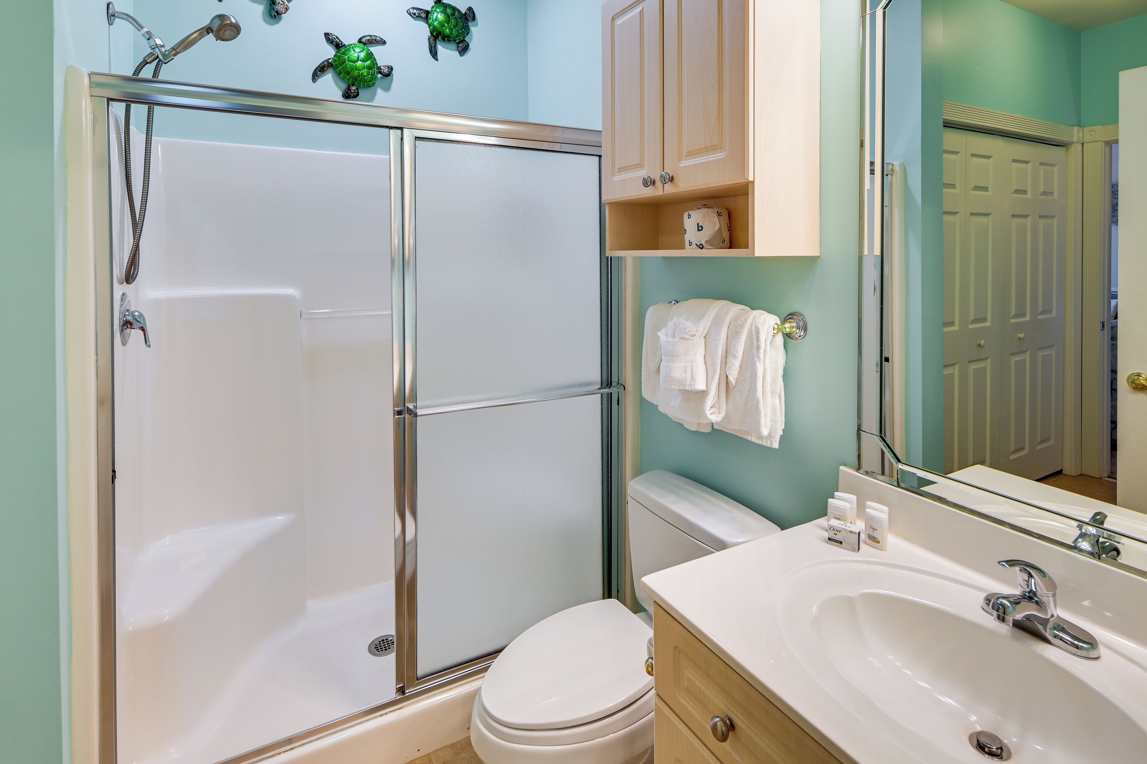 A bathroom with a glass-enclosed shower, a white toilet, a sink with a mirror, and a towel rack.