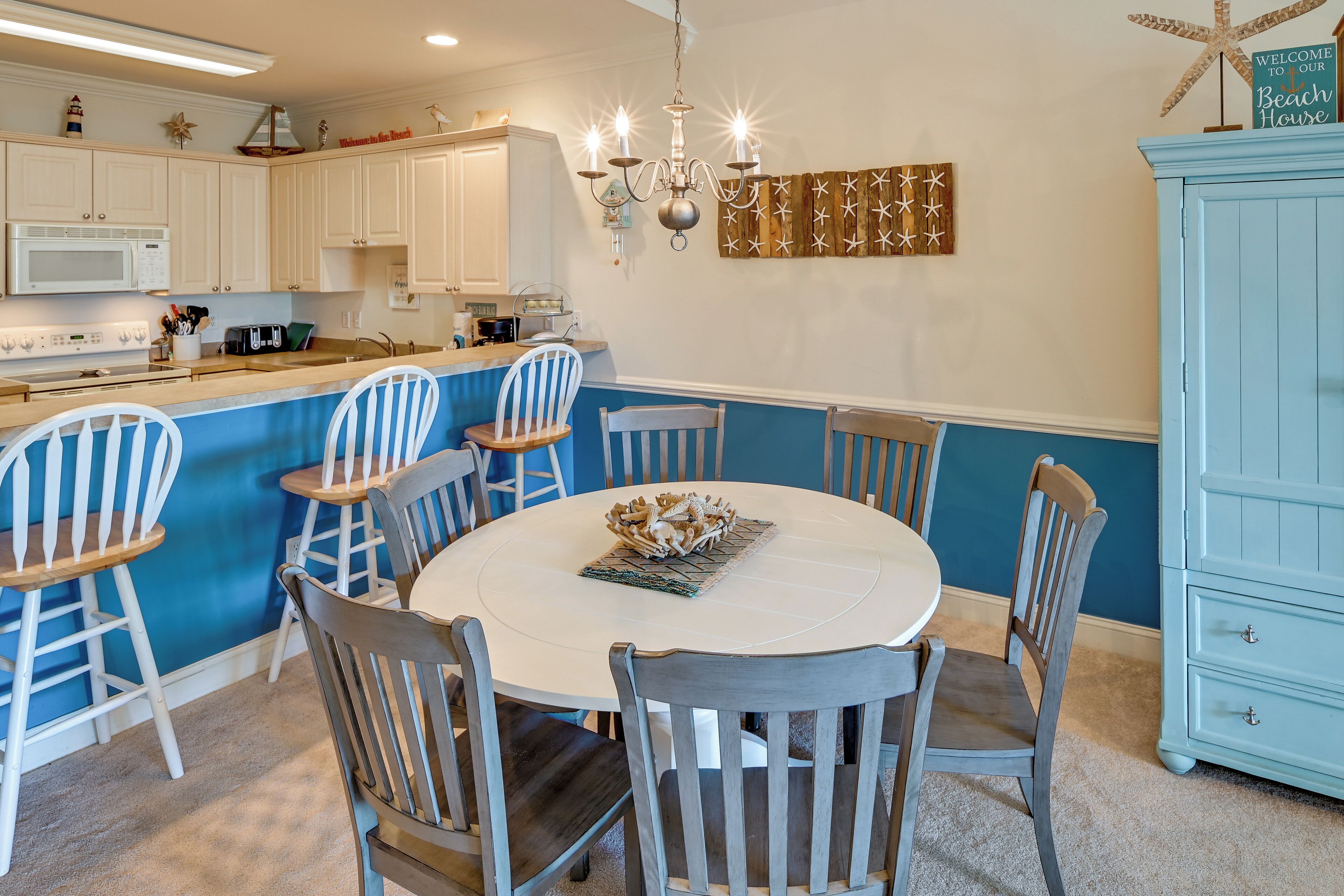 Une cuisine avec des meubles blancs, un mur d’accent bleu, une table de salle à manger ronde entourée de six chaises, et un meuble bleu.
