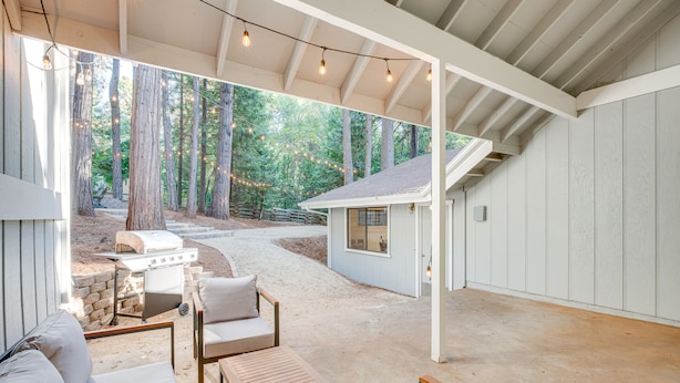 An outdoor patio area with a grill, seating, and a view of a forest. - Pollock Pines Cabin: Game Room w/ A/C & Heat! (Pollock Pines)