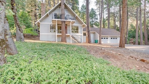 A two-story cabin with a balcony, surrounded by tall trees and a well-maintained garden. - Pollock Pines Cabin: Game Room w/ A/C & Heat! (Pollock Pines)