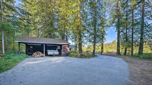 A cabin with a gravel driveway, surrounded by tall trees and a hammock. - Dreamy Riverside Cabin With Fireplace & Grill (Concrete)