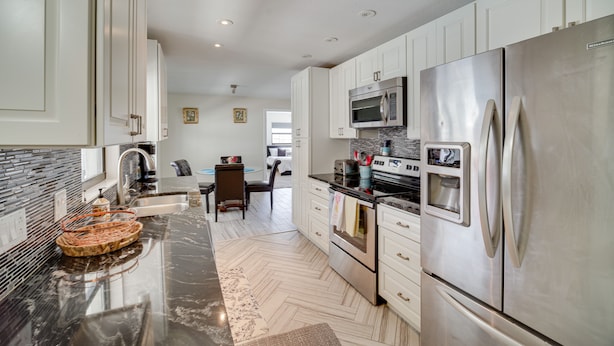 A modern kitchen with stainless steel appliances, white cabinetry, and a herringbone floor pattern. - 'space Coast' Getaway w/ Outdoor Pool & Spa! (Palm Bay)