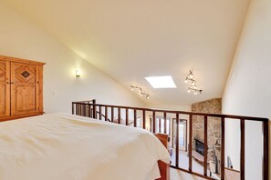 A bedroom with a large bed, wooden wardrobe, and a stone fireplace. - Private Balcony & Mtn Views: Granby Studio! (Granby)