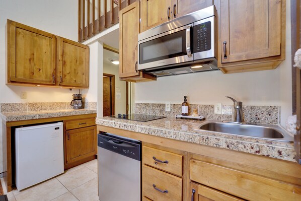 A kitchen with wooden cabinets, a stainless steel microwave, a dishwasher, and granite countertops. - Private Balcony & Mtn Views: Granby Studio! (Granby)