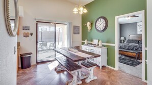 A room with a wooden dining table, benches, a chandelier, a clock, a cow skull decoration, a bed, and a sliding glass door leading to an outdoor area. - Inviting Bullhead City Gem: 3 Mi to Colorado River (Bullhead City)