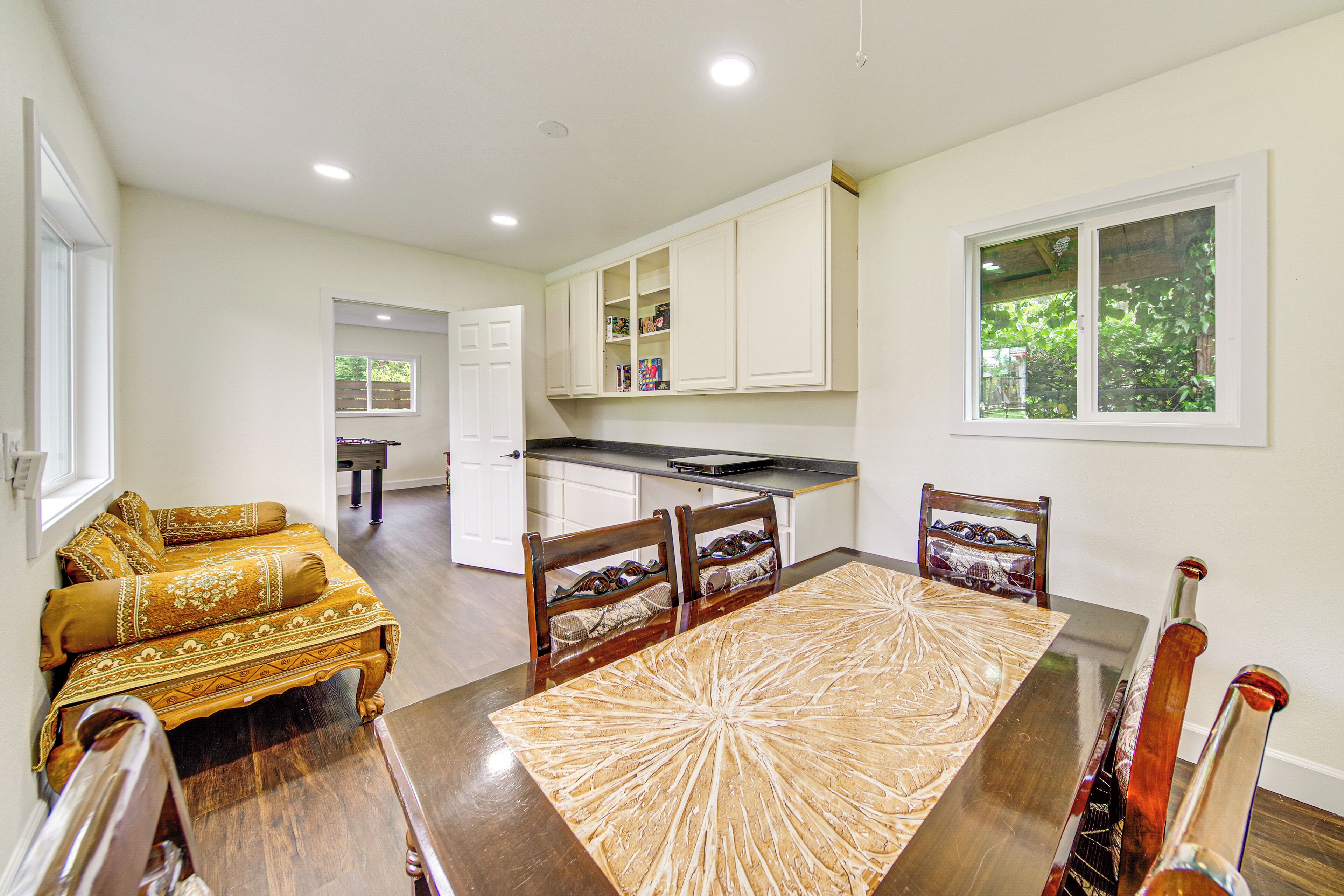 A dining area with a large wooden table, four chairs, and a sofa with patterned cushions.