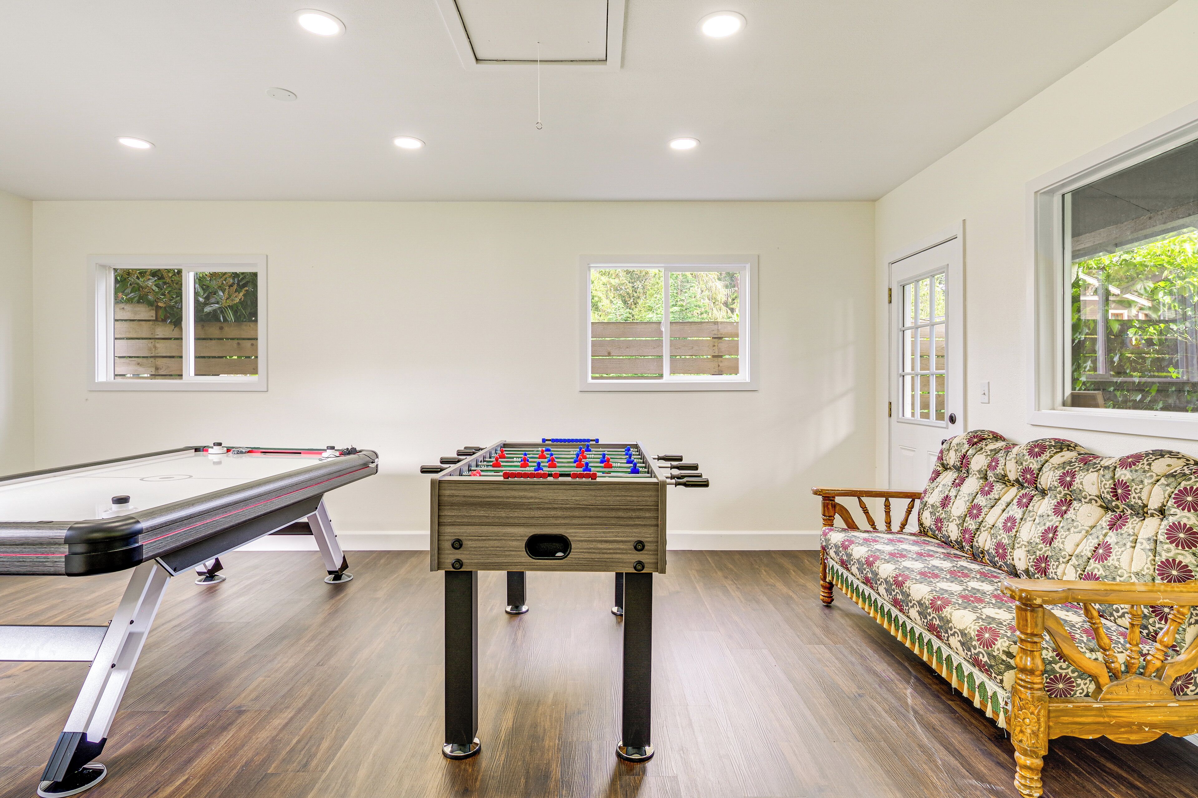 Una habitación con mesa de futbolín, un sofá y dos ventanas.