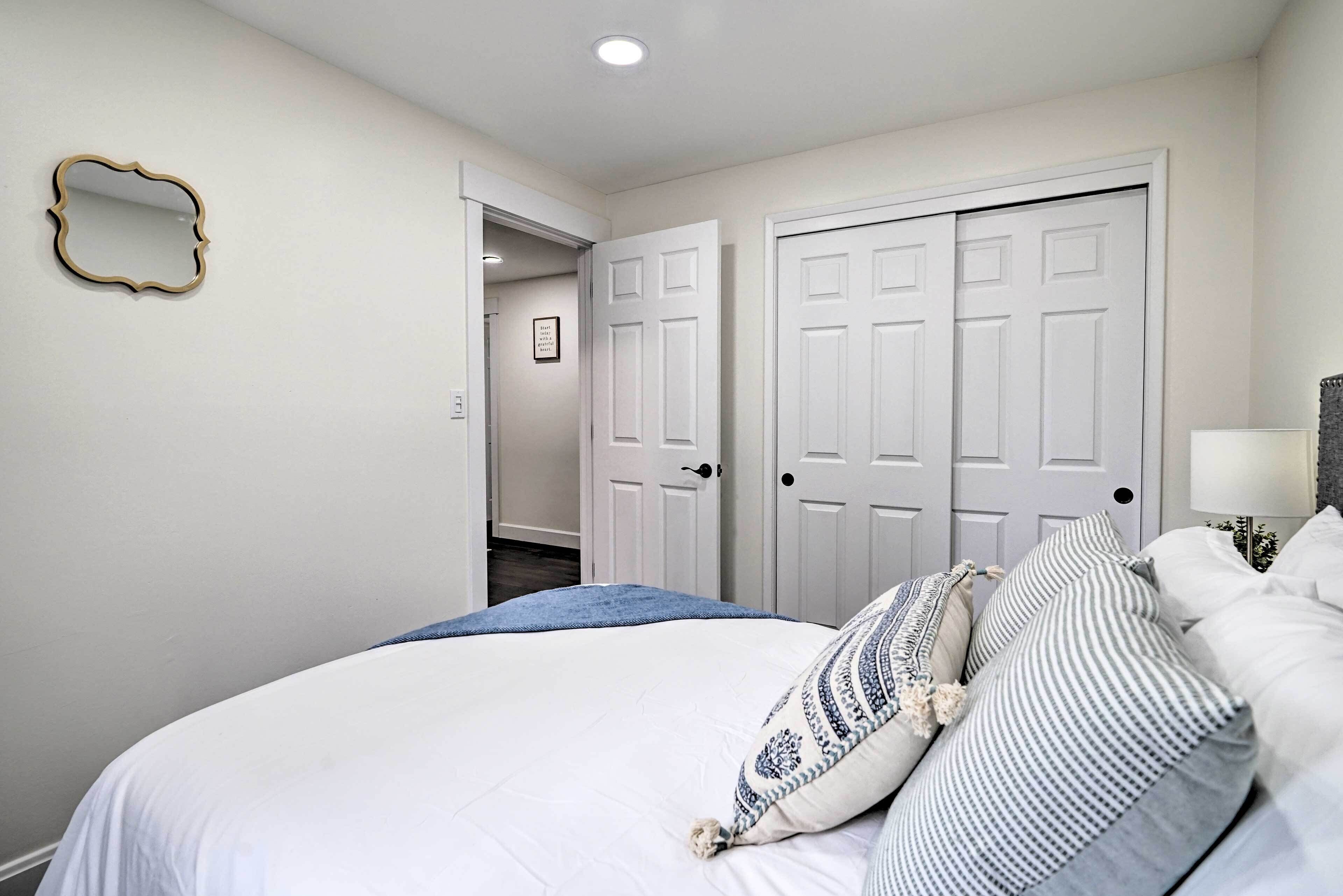 A bedroom with a large bed, two white doors, a mirror, and a hallway leading to another room.
