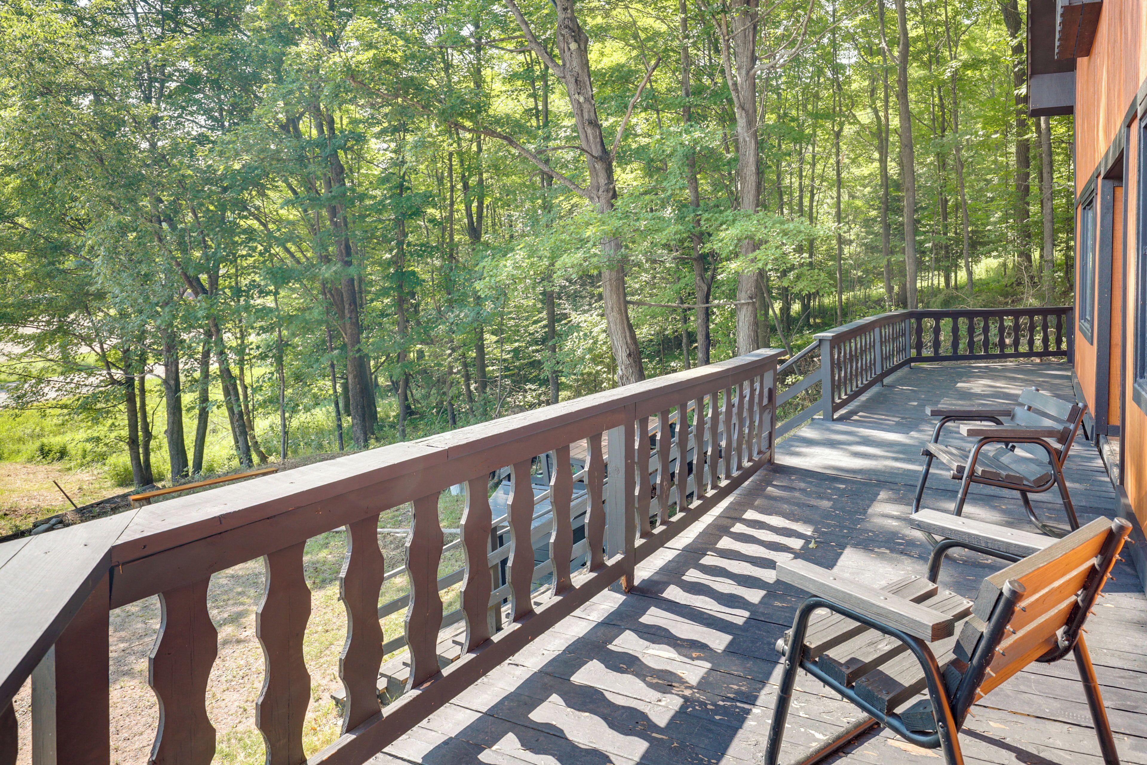 A wooden deck with a railing, benches, and a view of a forested area.