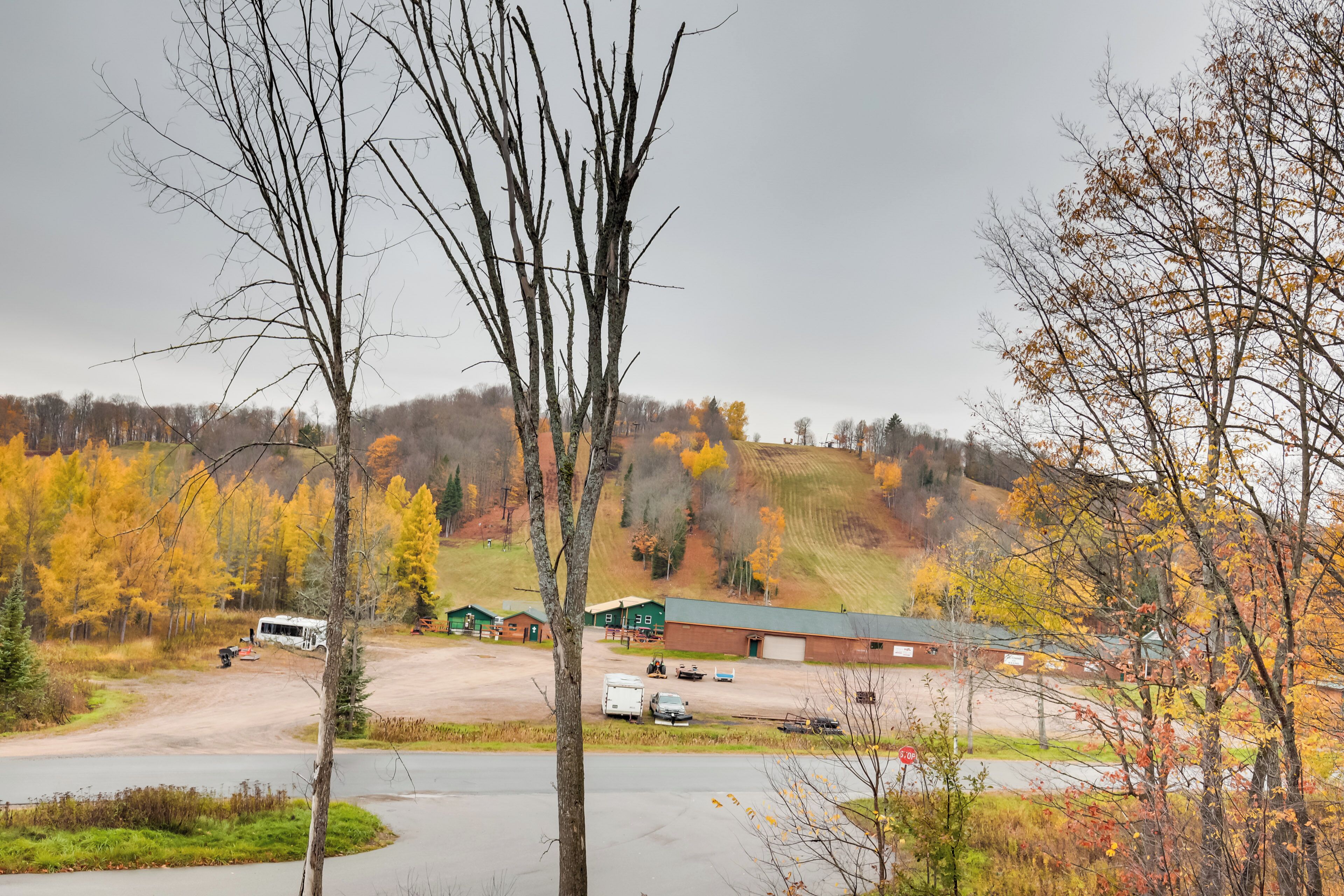 A rural landscape with a parking area, a green building, and autumn-colored trees.