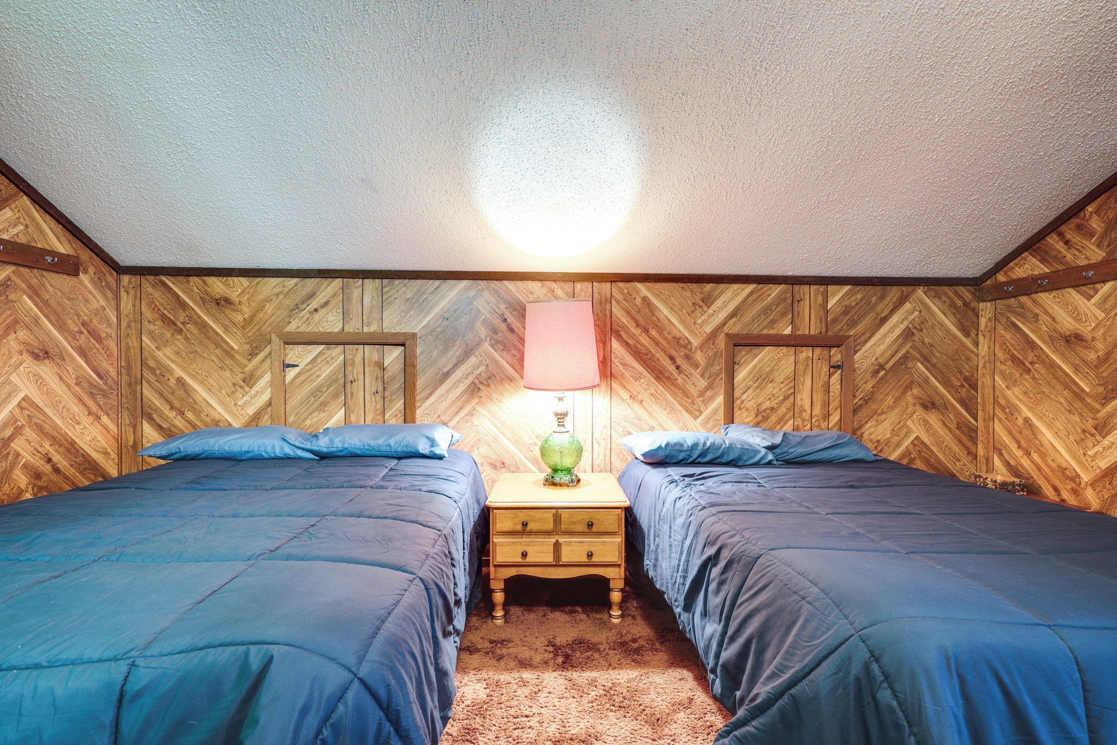 Ein Zimmer mit zwei Betten, Holzwandverkleidung, einem Nachttisch mit Lampe und einer Deckenleuchte.