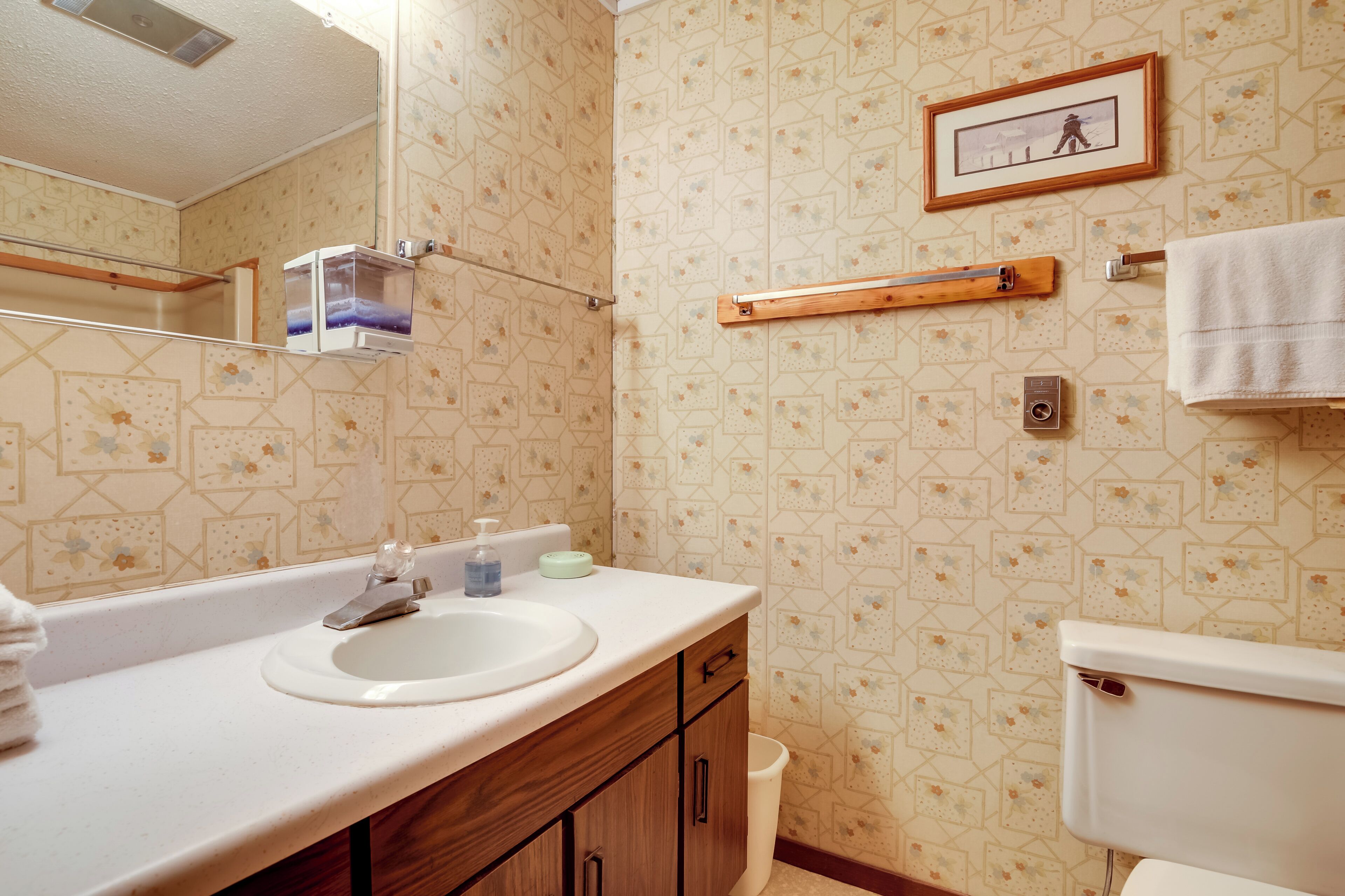 Un baño con lavamanos, espejo, armarios de madera, inodoro y zona de ducha.