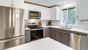 A modern kitchen with stainless steel appliances, white cabinets, and a large window providing natural light. - Beautiful Kenmore Retreat Near Marina & Beach! (Kenmore)